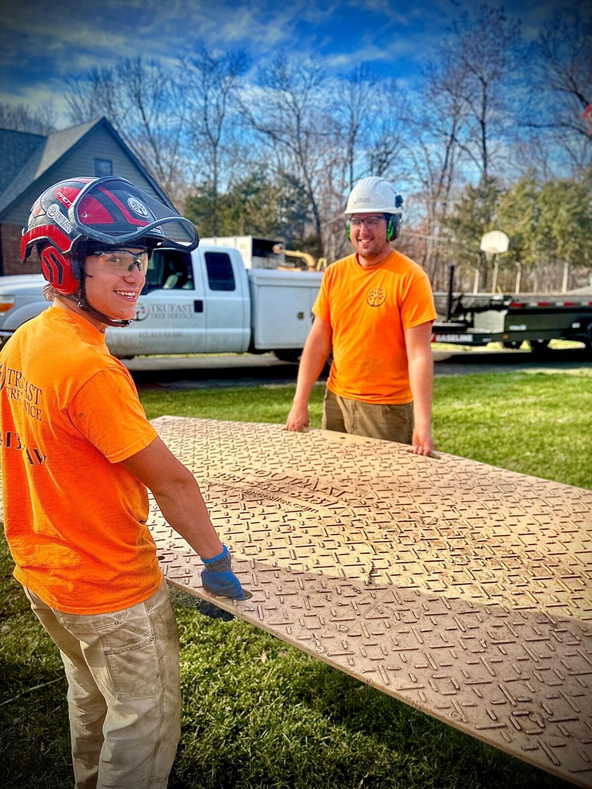 Two crew carrying ground-protection mat past truck