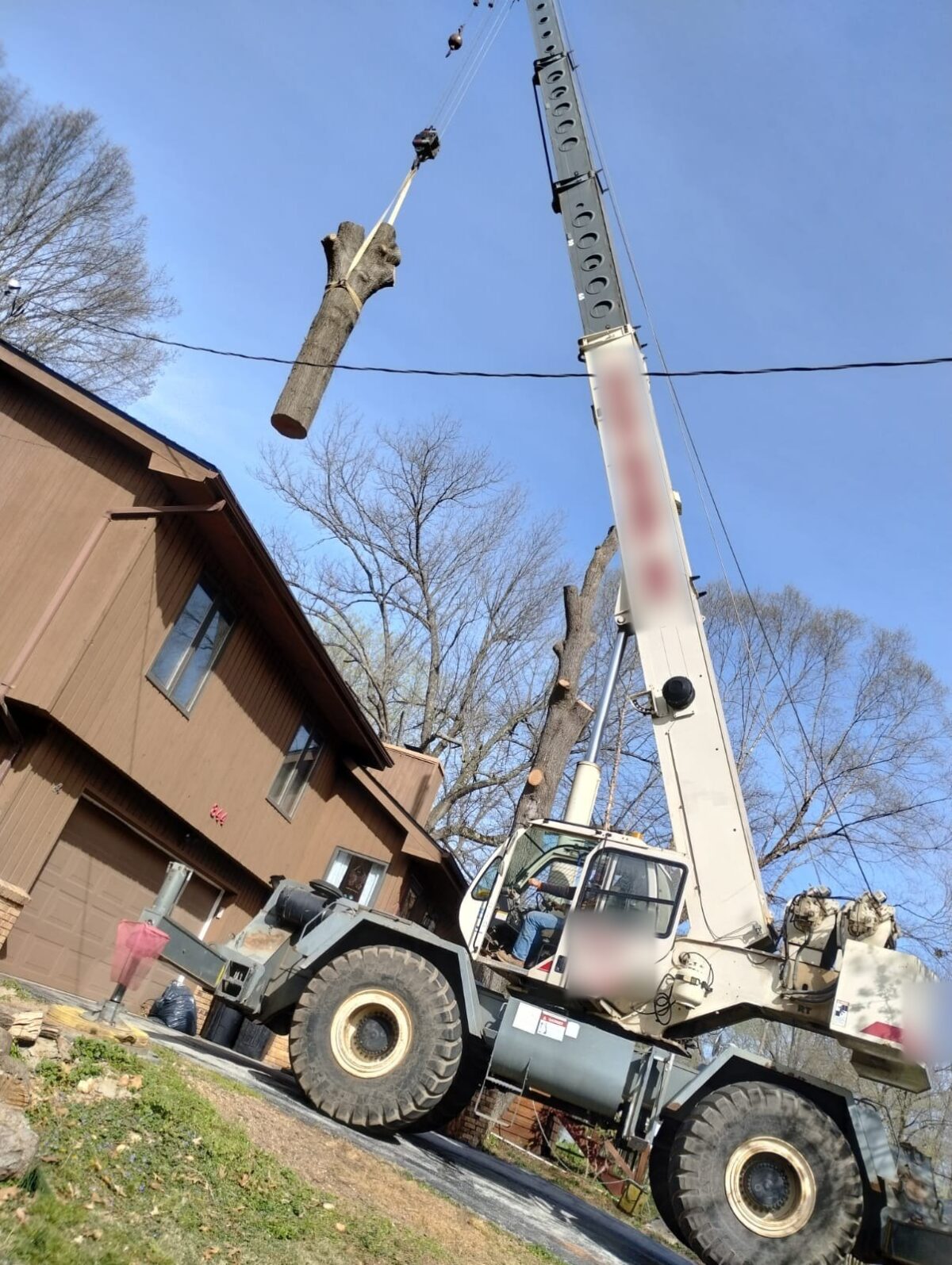A crane lifting a cut trunk section away from a house during a Trufast removal.