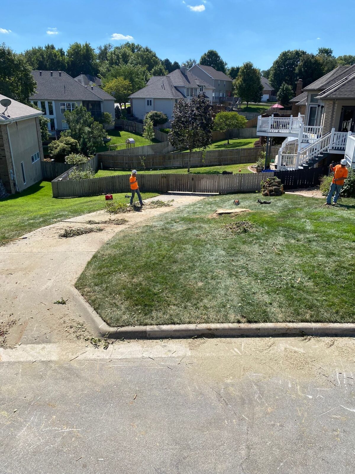 Two Trufast crew cleaning up after a tree removal in a tidy subdivision, sawdust swept from the drive and lawn.
