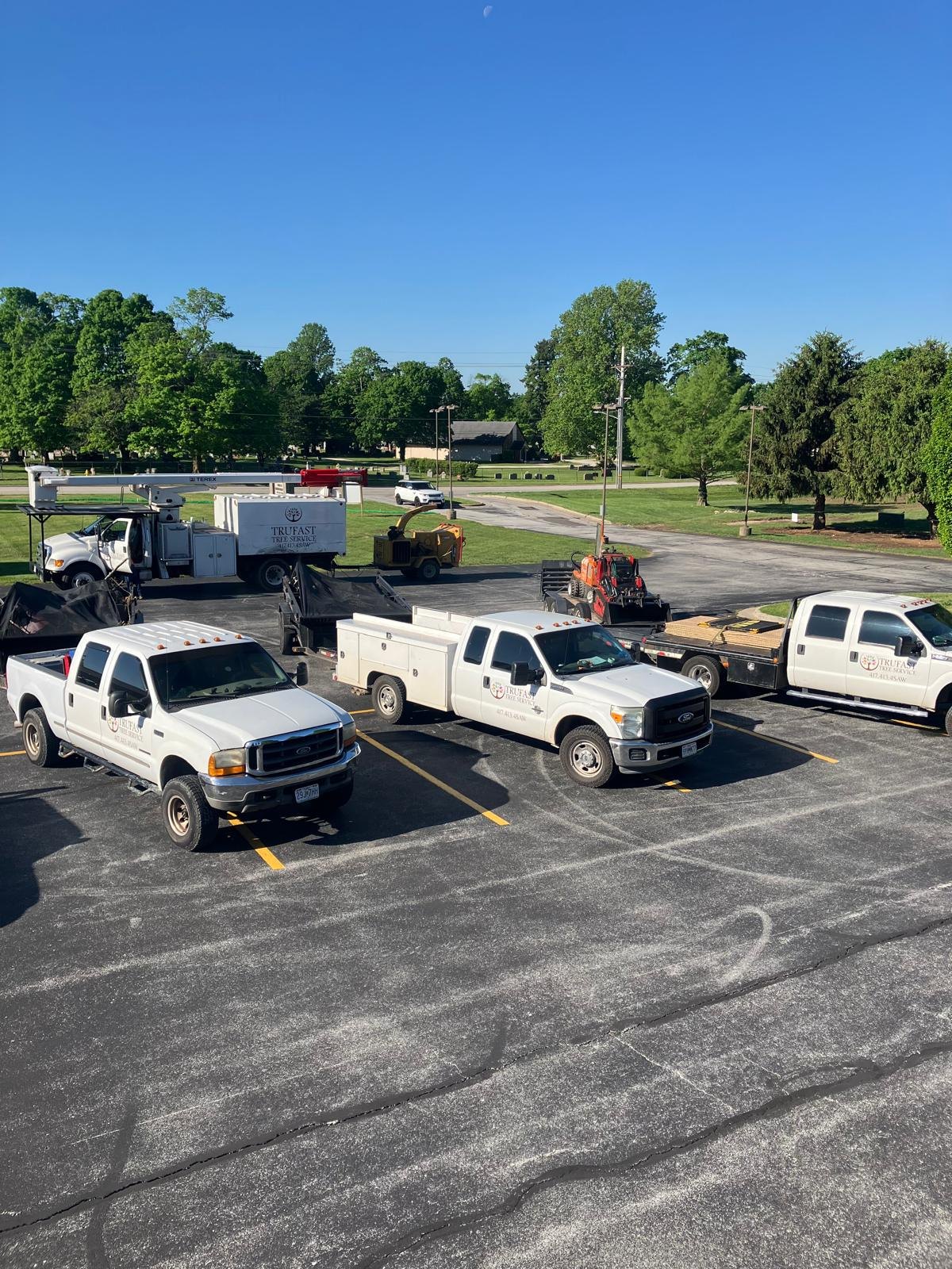 The Trufast fleet of lettered pickups, a bucket truck and a chipper parked in a lot.