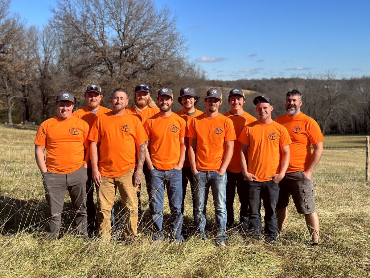 Ten Trufast crew members in orange shirts and caps standing together in a field.