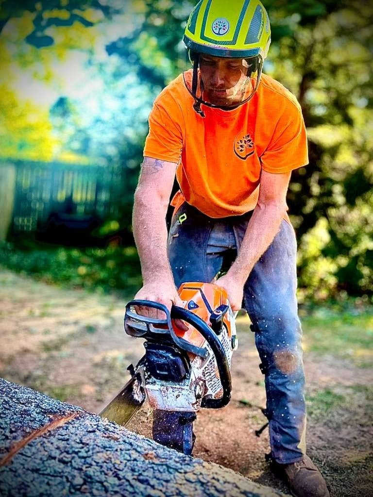 Matthew Crider, Trufast crew lead, in a helmet and face shield bucking a log with a chainsaw