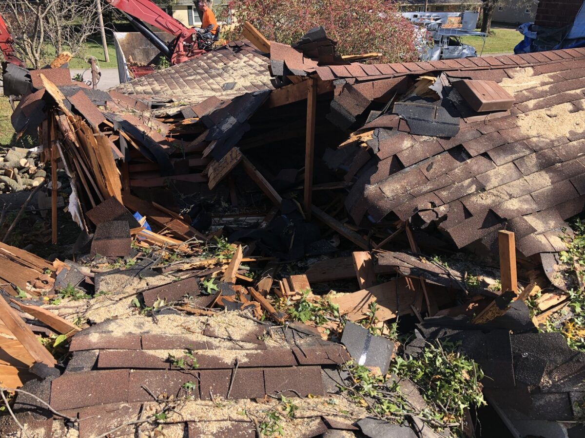 A house roof caved in after a tree fell on it, with broken rafters and shingles, Trufast crew and equipment working beyond