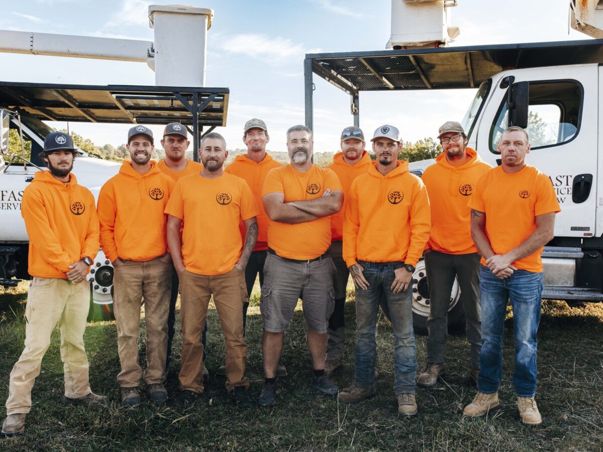 Ten Trufast crew members in orange Trufast shirts and hoodies standing in front of two bucket trucks