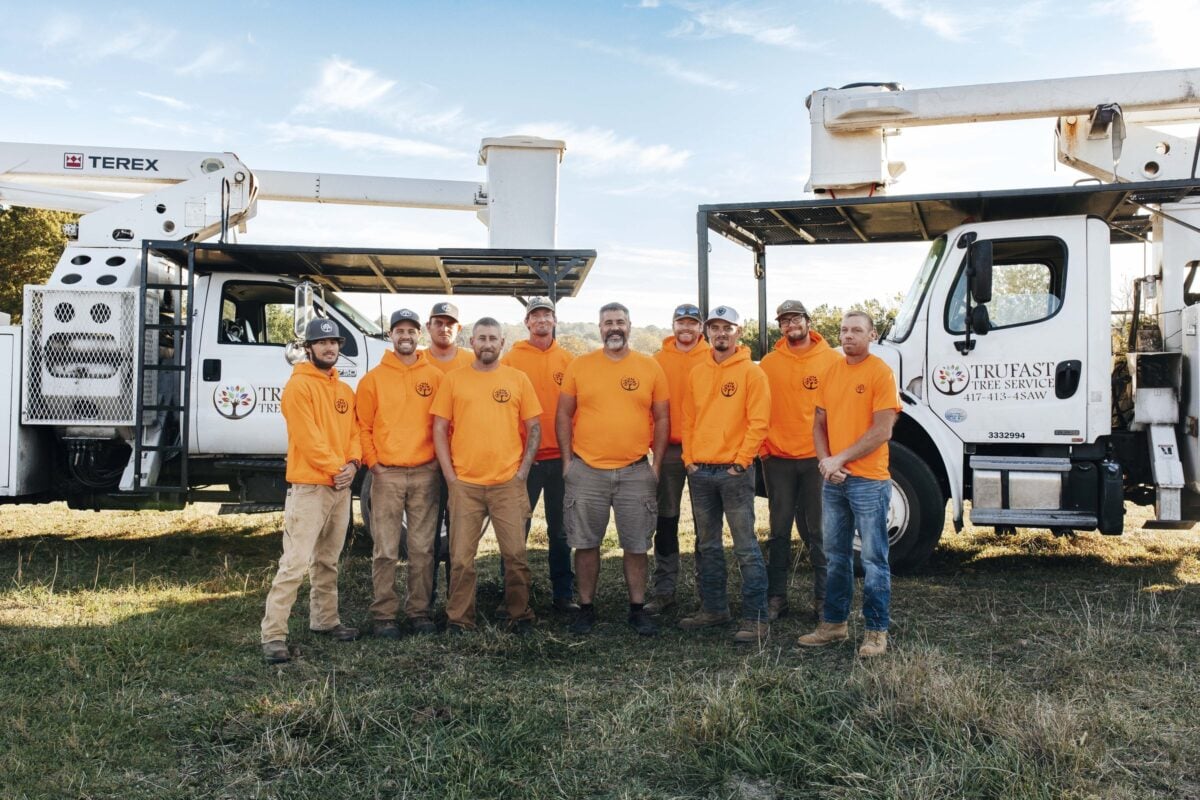 Ten Trufast crew members in orange shirts standing between two bucket trucks