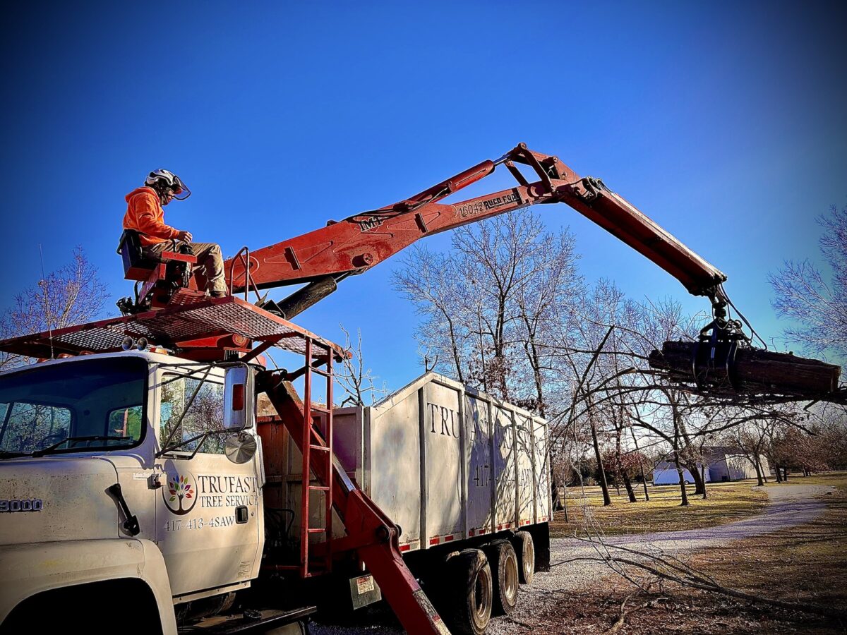 Trufast crew member at the controls of the lettered grapple truck, swinging a load of logs into the dump bed