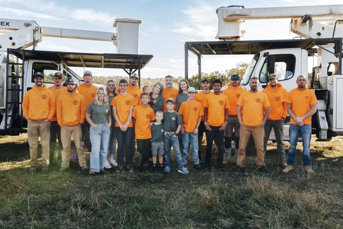 The Trufast crew, office staff and their kids together in a field between two bucket trucks